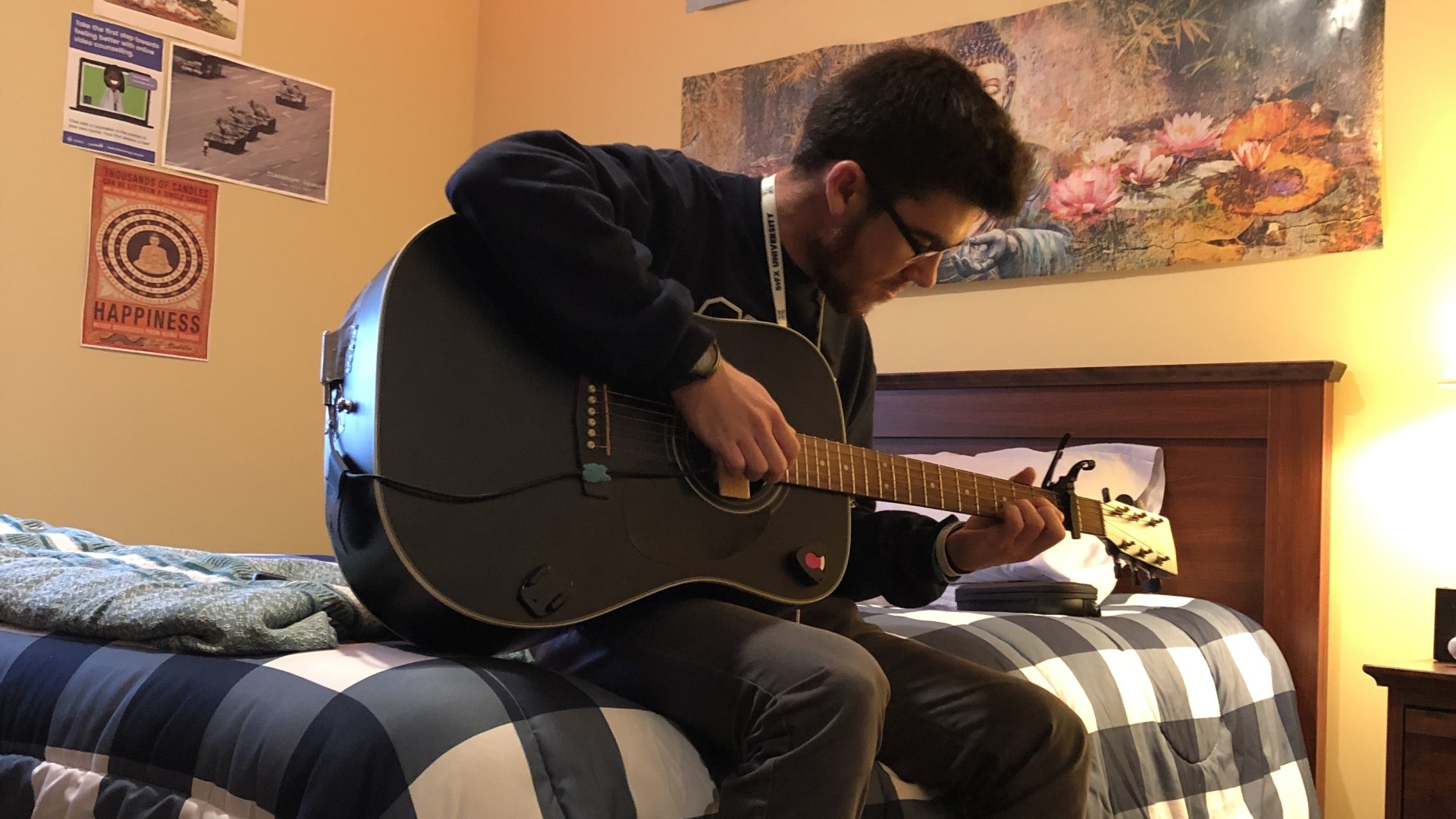 Student sitting on their bed while playing the guitar in Riley Hall.