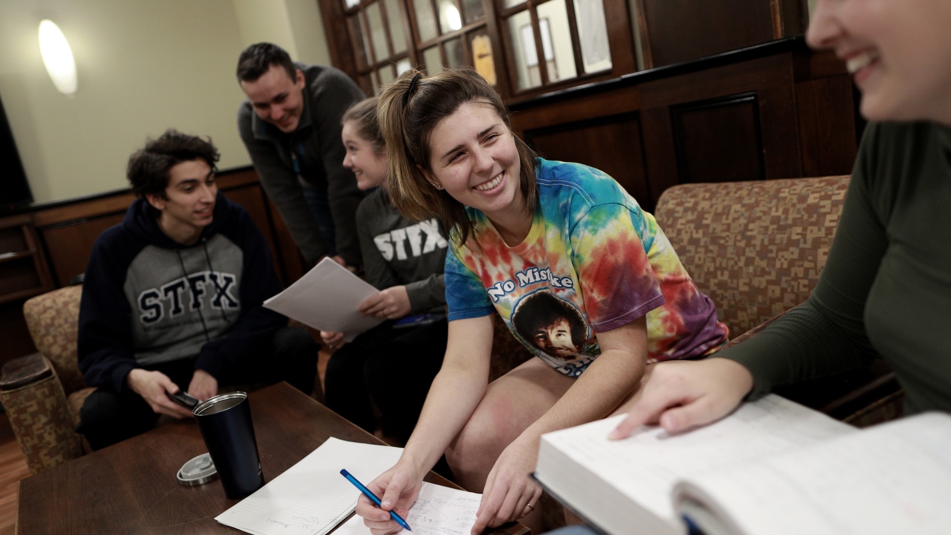 Students studying in the Bishops Hall lounge area. They are sitting on couches, using a table in the center for their notes.