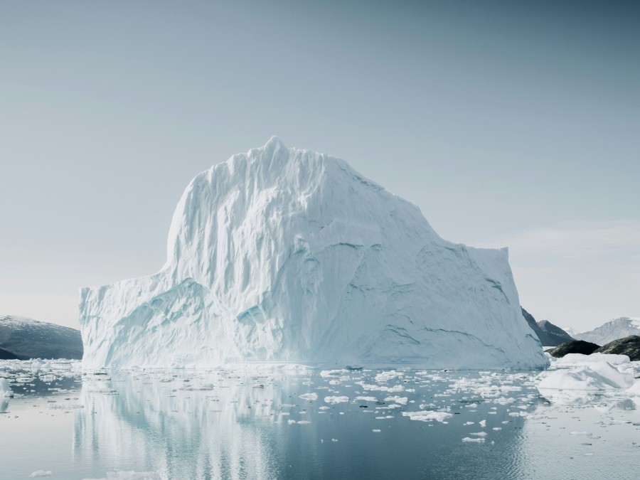 Large iceberg on water against a cloudy sky.